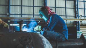 A welder working on a large steel structure inside a fabrication workshop, demonstrating industrial steelwork and connection techniques used in modern construction