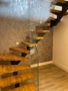 Bespoke floating wooden staircase with central steel spine and structural glass balustrade fabricated by Has Metal Work.